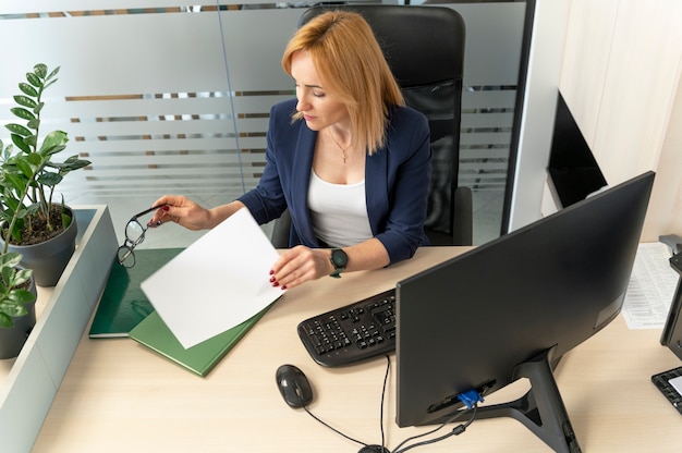 A person sitting at a desk, reviewing documents related to grant applications on a computer. There are folders and papers organized around them, suggesting a focused and diligent approach to understanding eligibility requirements.