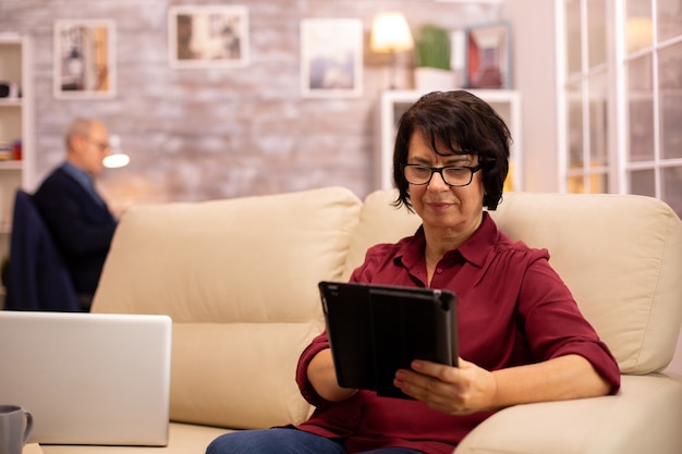 A veteran using a tablet for a telehealth appointment, smiling and engaged. The background is a comfortable living room setting.