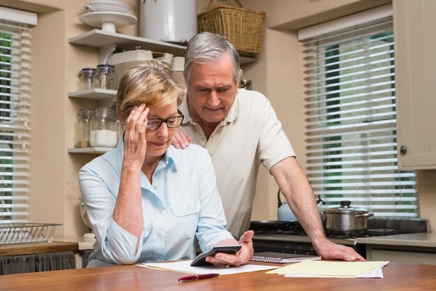 A senior couple reviewing their medication bills at home, looking concerned.