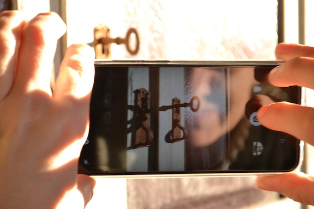 A close-up of a person's hand placing a padlock on a smartphone screen. The background is blurred, focusing on the padlock and phone.