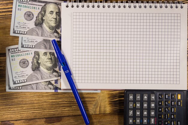 A stack of U.S. currency bills next to a calculator and a pen, symbolizing financial planning and tax preparation for the upcoming year. The scene includes a balanced composition with elements like a calendar marked for April 15th (tax day) and a small model of a house, representing homeownership and associated tax benefits.