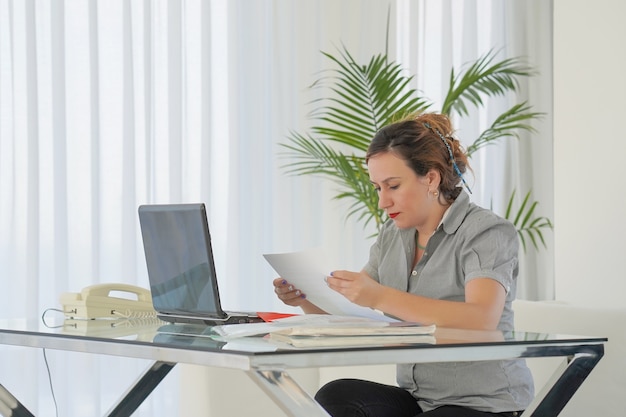 A person sitting at a desk, reviewing financial documents and using a laptop, with a focus on tax-related topics. The setting is an organized and well-lit home office, emphasizing the attention to detail required for accurate tax filing and planning.