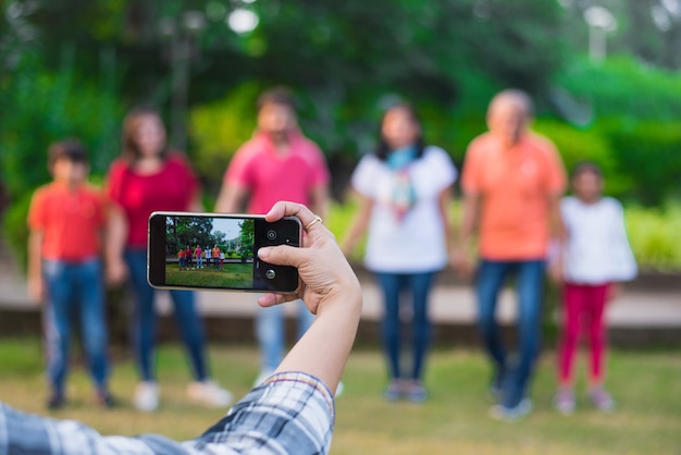 A diverse group of young people gathered in a public park, all filming themselves performing the same dance challenge on their smartphones, showing community and shared activity.