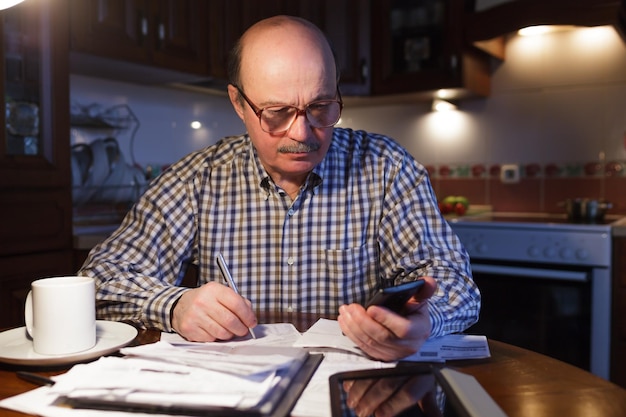 A close-up of a hand using a calculator while reviewing a stack of bills, with a serious expression.