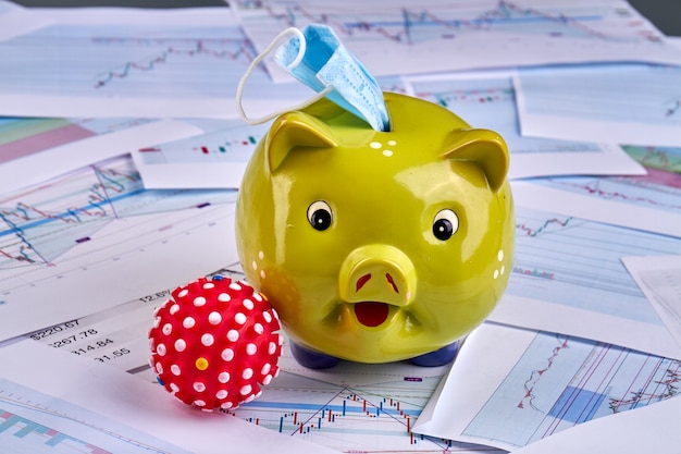 A close-up of a piggy bank sitting on top of financial newspapers and stock charts.